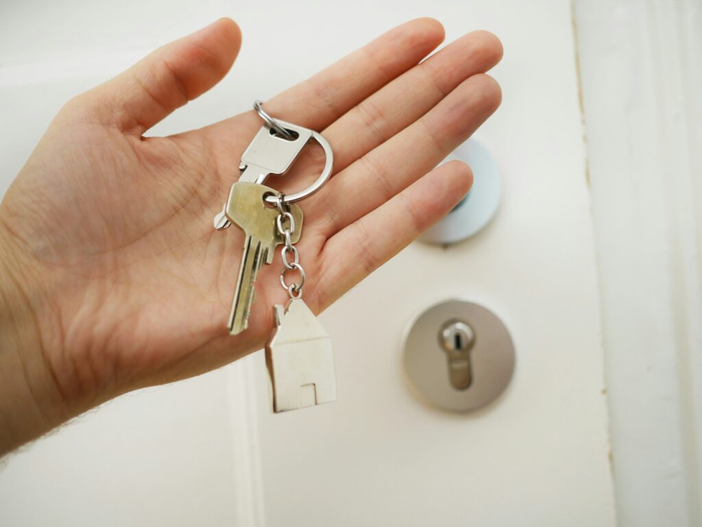 Hand met sleutels bij de deur, symbool voor sleuteloverdracht van een woning.